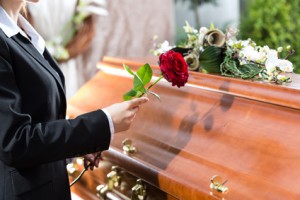 Mourning woman on funeral with red rose standing at casket or coffin